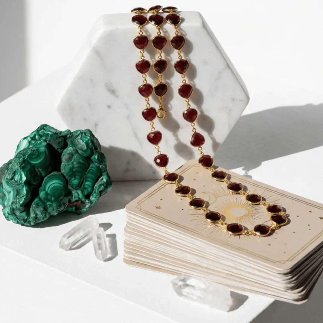 Jewelry set with red beads and gold accents on a card, next to a green stone and crystal on a white surface.