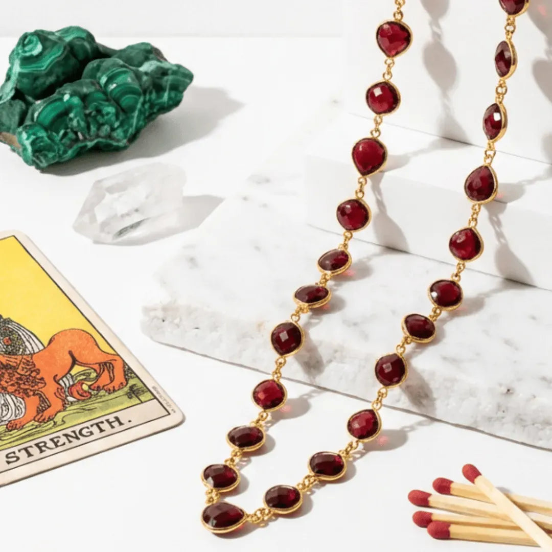 Garnet necklace on a white surface with tarot card, crystals, and matches.