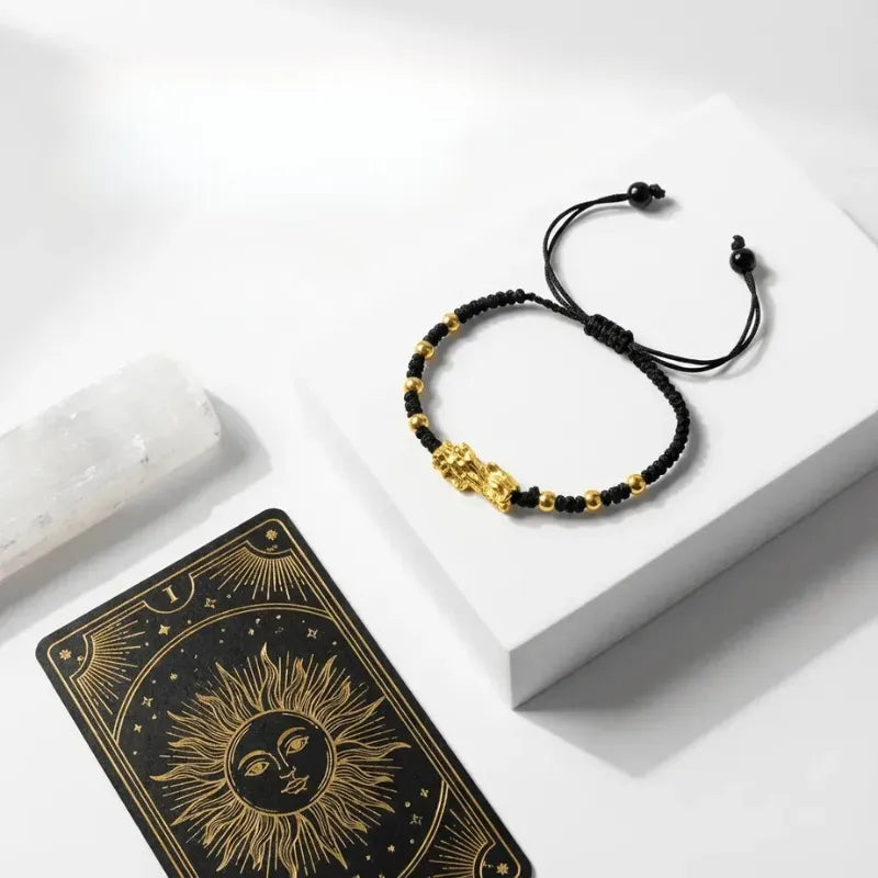 Black and gold beaded bracelet on a white surface with a tarot card featuring a sun design.
