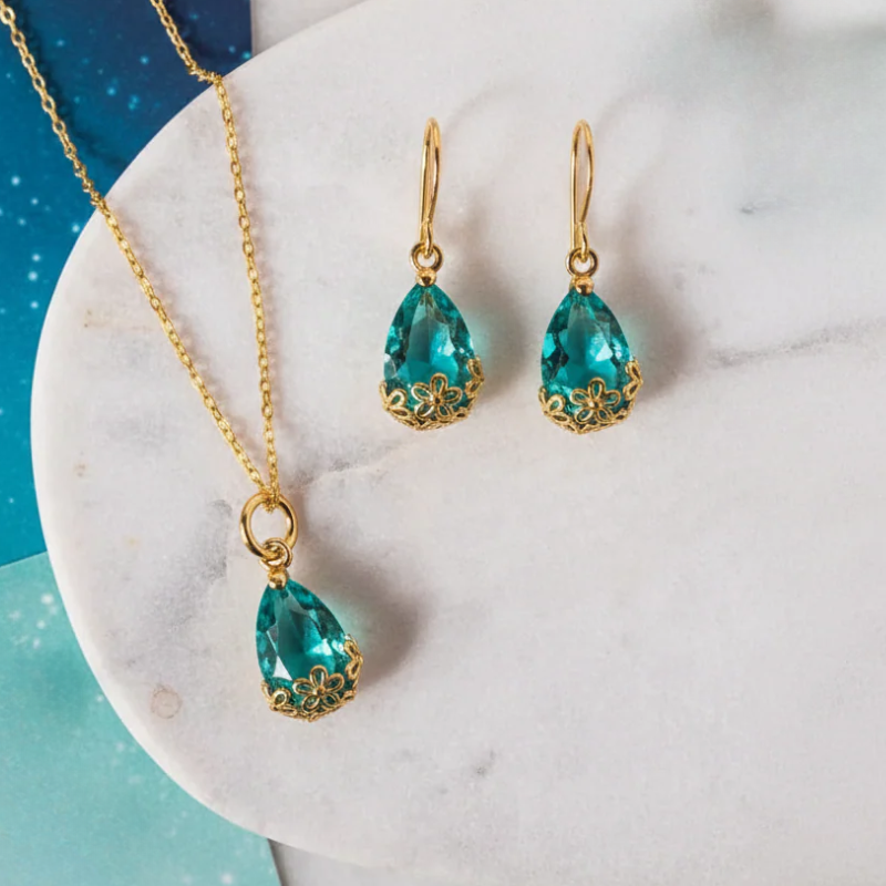 Gold jewelry set featuring a necklace and matching drop earrings with faceted teal-blue teardrop