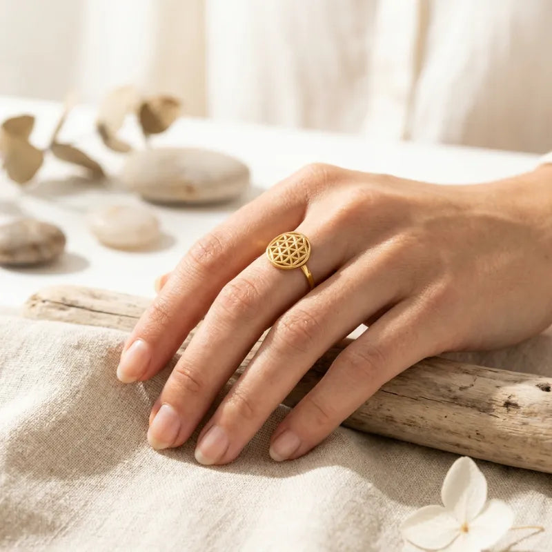 Hand wearing a gold ring on a natural setting with stones and driftwood.