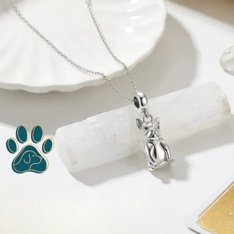 Silver pendant of a dog on a chain, placed on a white surface with a paw print logo.