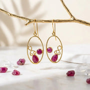 Gold earrings with red gemstones on a branch with more gemstones below.