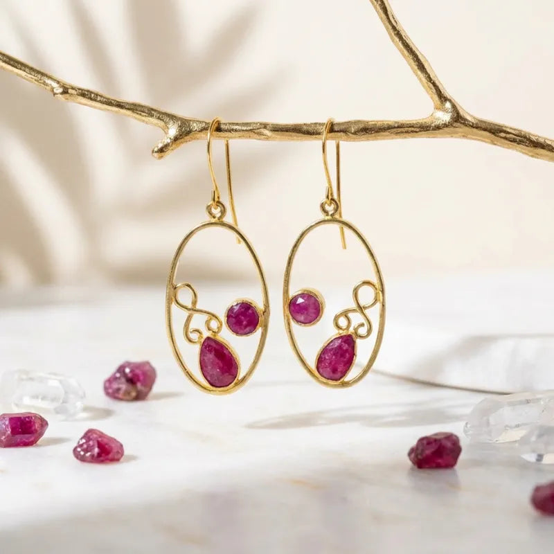 Gold earrings with red gemstones on a branch with more gemstones below.