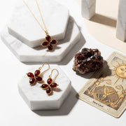 Gold jewelry with red stones on marble stands, next to a tarot card.