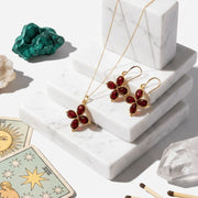 Jewelry set with red gemstones on a marble surface with crystals and tarot cards.
