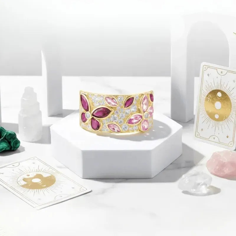 Decorative bracelet with pink and gold accents on a white surface with cards and small sculptures.