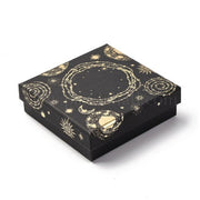 Black celestial gift box with gold foil sun and moon print, open to show a gold necklace on black velvet, beside a teal satin pouch and handwritten note card