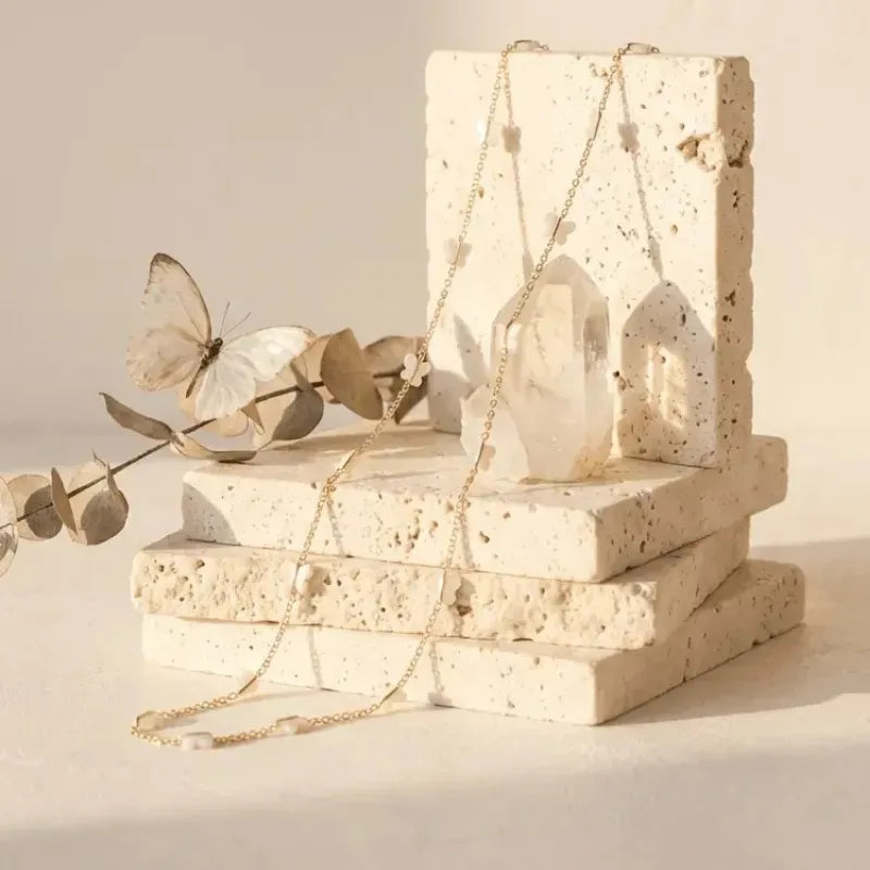Necklace displayed on a stone block with a butterfly and leaves in the background