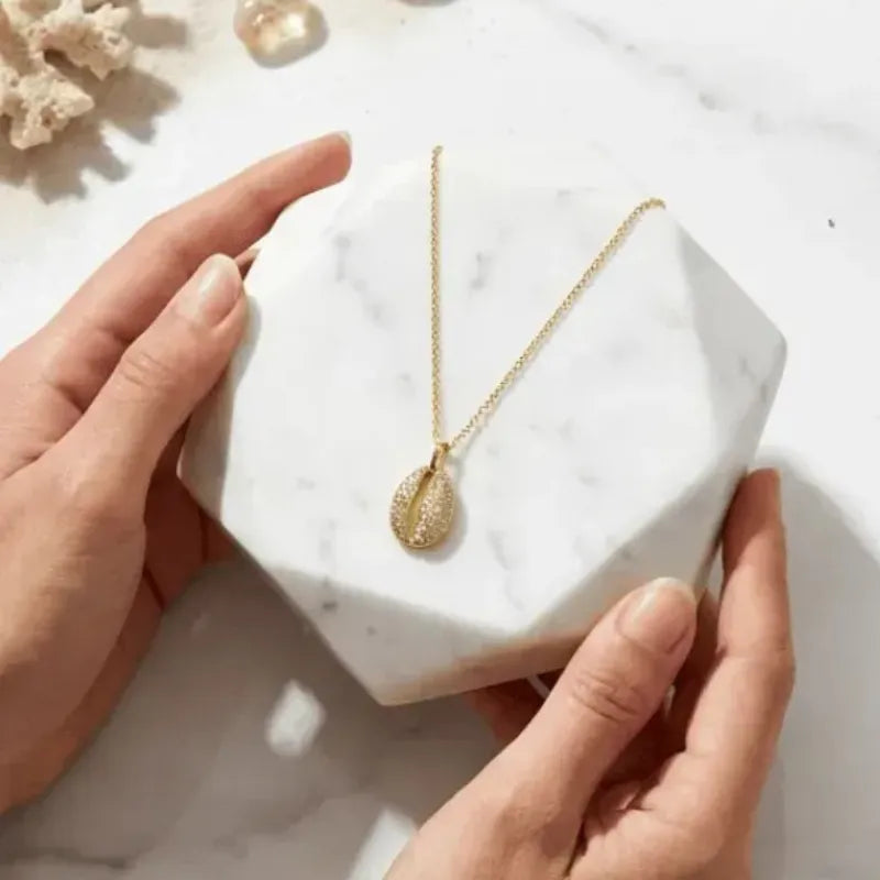 Gold necklace on a white marble block held by hands with a light background