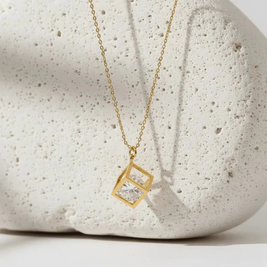 gold necklace hanging against a white stone with white background