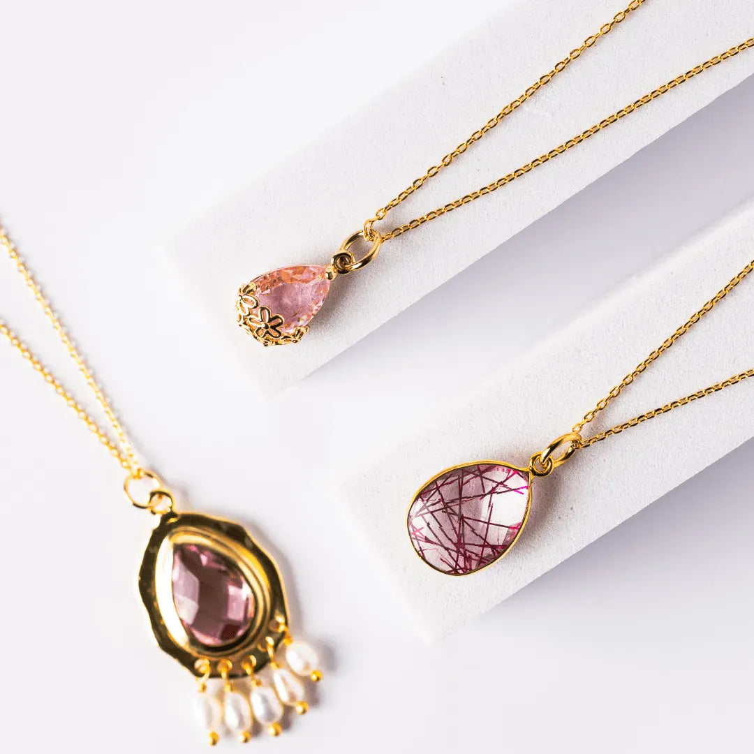 Two gold necklaces with pink gemstone pendants on a white background