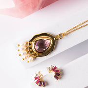 Pink teardrop earrings with gold hooks hanging from a branch on a white background