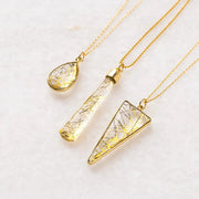 Three gold necklaces with crystal pendants on a light background