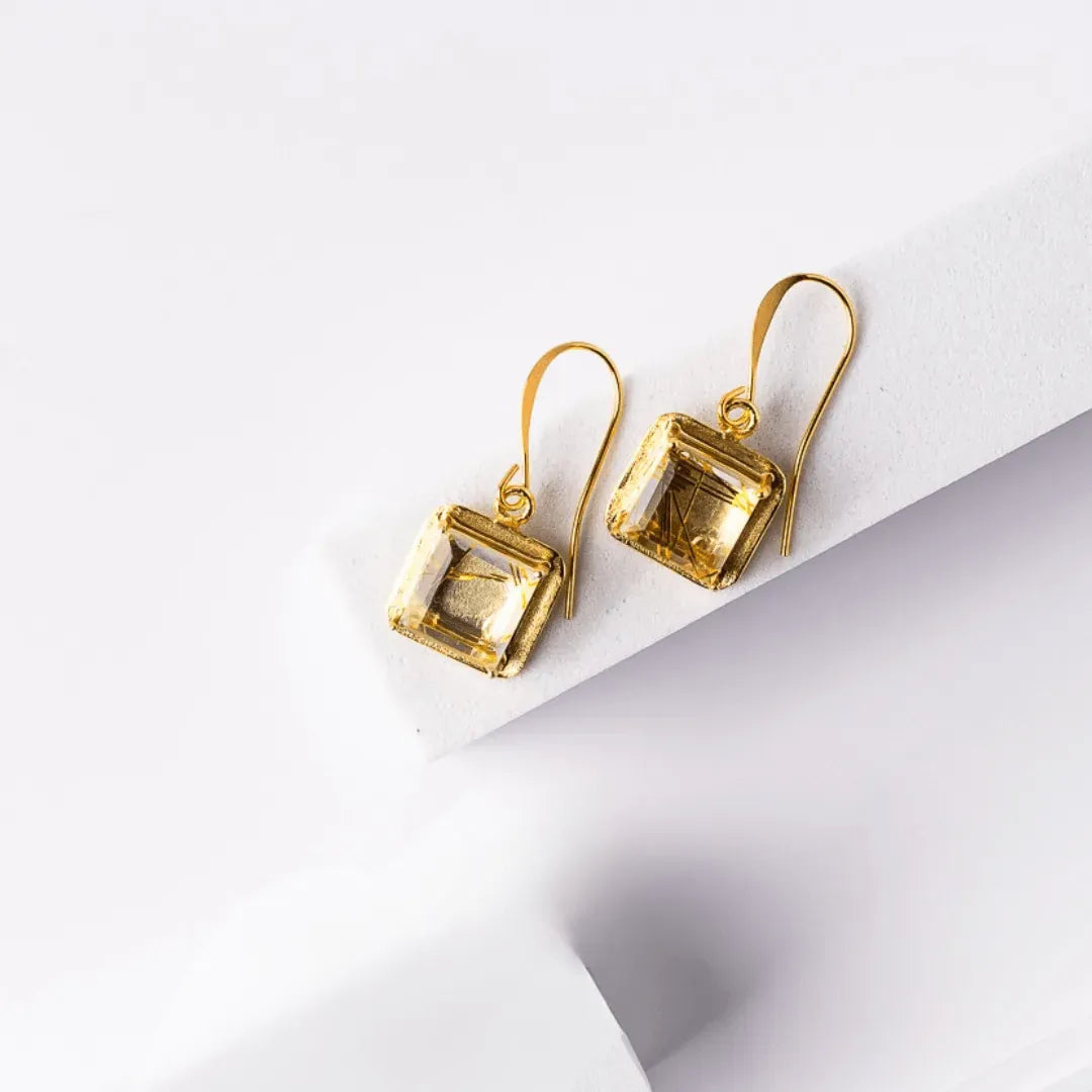 Gold earrings with square gemstones on a white background