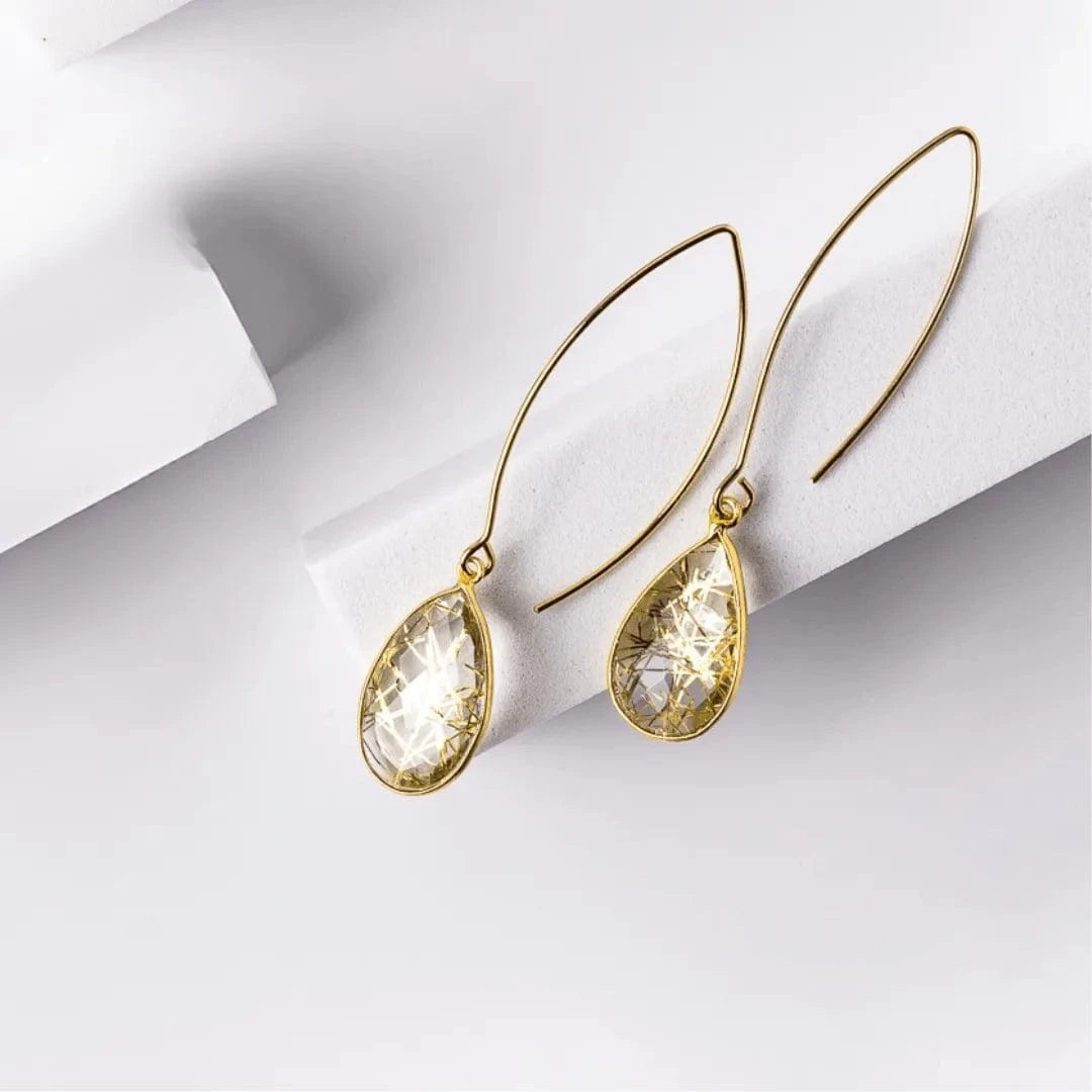 Gold earrings with clear gemstones on a light gray background