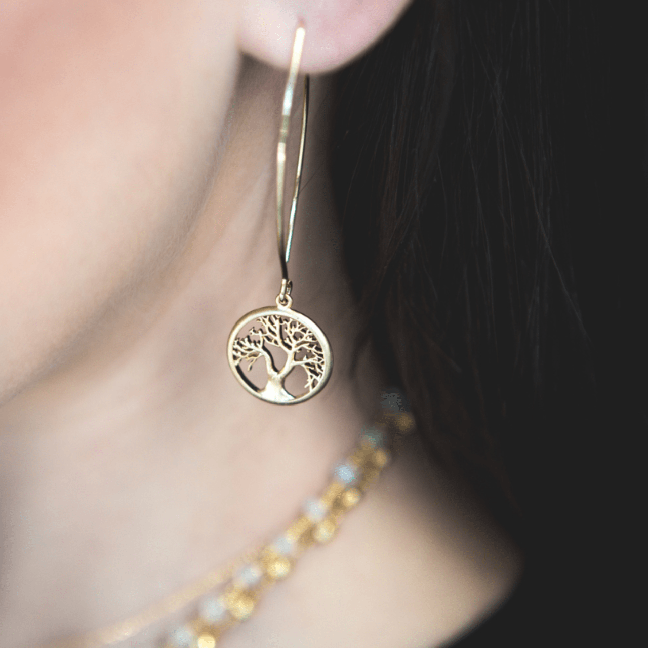 Gold earring with tree design worn by a person