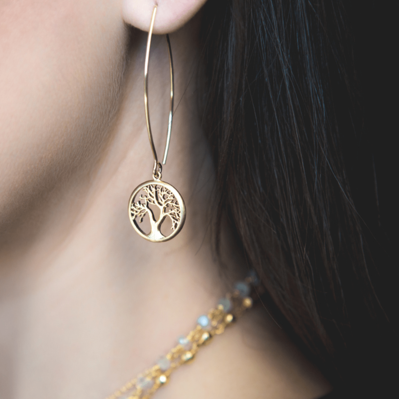 Gold hoop earring with tree of life design worn by a person.