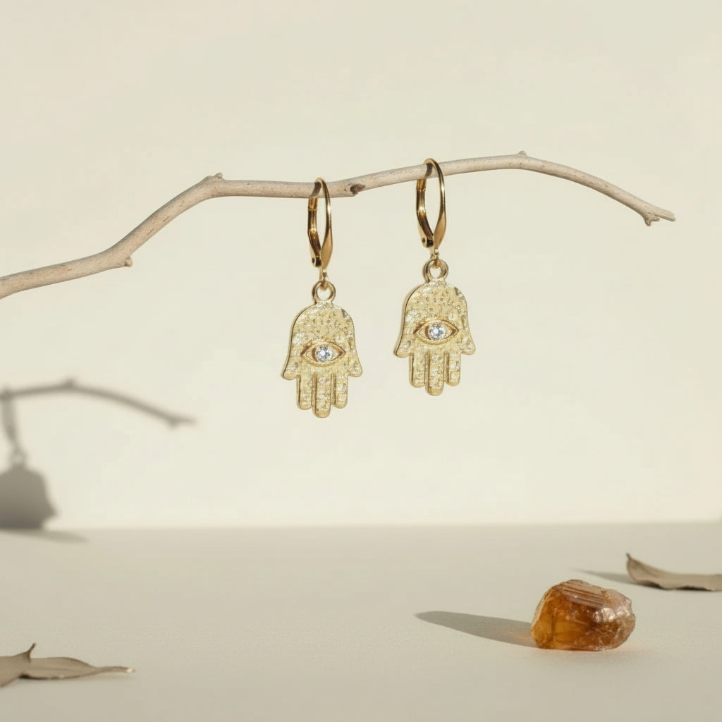 Gold plated hamsa hand earrings with eye detail hanging from a driftwood branch