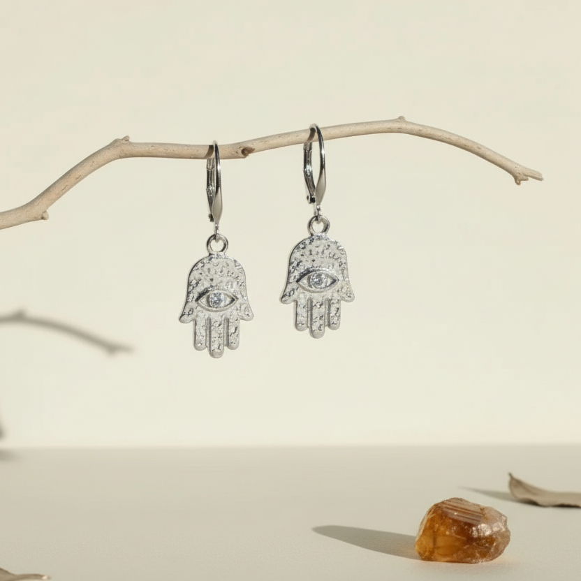 Silver plated hamsa hand earrings with eye detail hanging from a driftwood branch