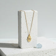 Large gold plated hamsa hand necklace hanging on a white stone display