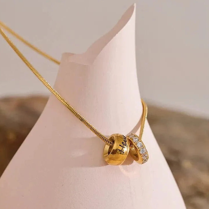 Gold necklace with a decorative pendant on a mannequin neck against a neutral background