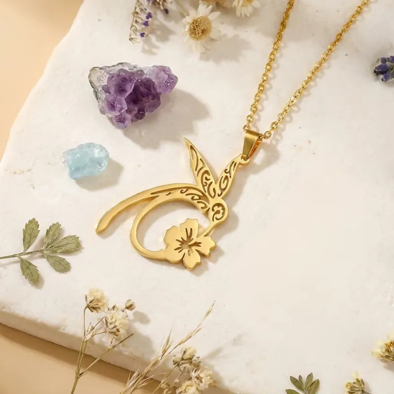 Gold necklace with a floral pendant on a white surface with crystals and flowers.