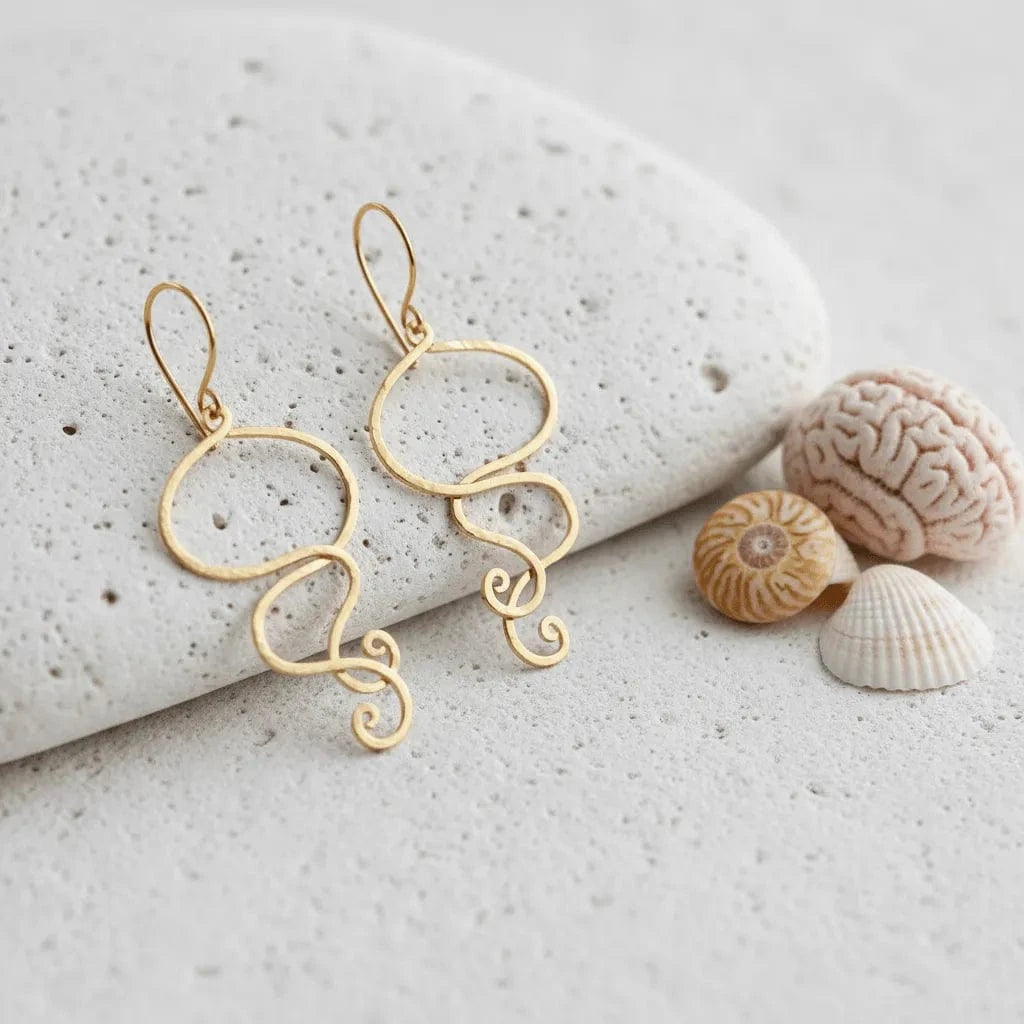 Gold earrings on a textured stone surface with seashells.