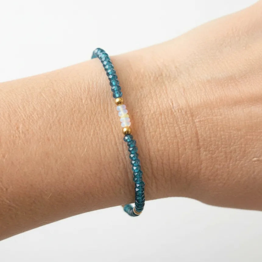 A close-up of a person's wrist wearing a delicate beaded bracelet. 