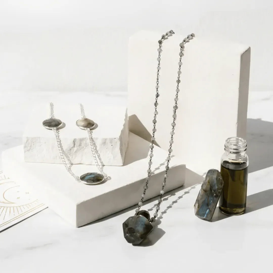 Necklace with labradorite stone pendant on a white surface with candles and a bottle.