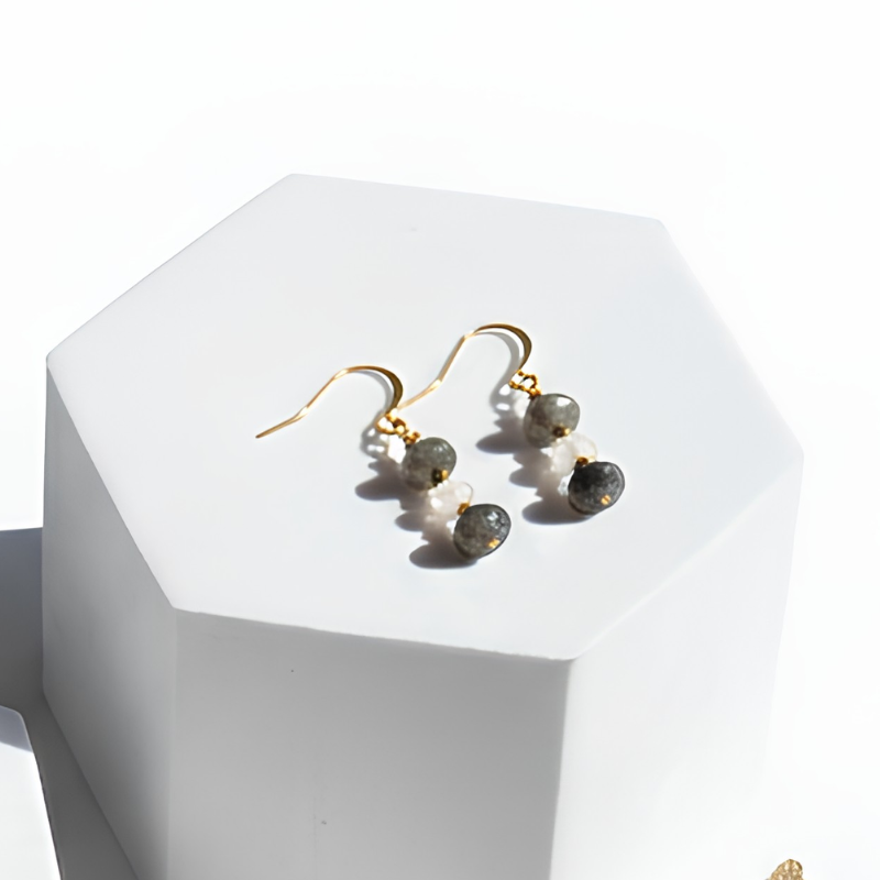 Gold earrings with green gemstones on a white hexagonal stand