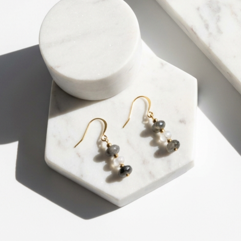 Gold earrings with black beads on a marble stand
