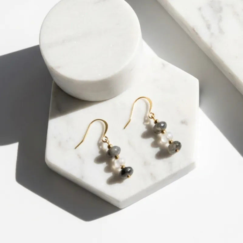 Gold earrings with black beads on a marble stand