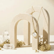 Necklace with a circular pendant hanging from a beige arch against a neutral background