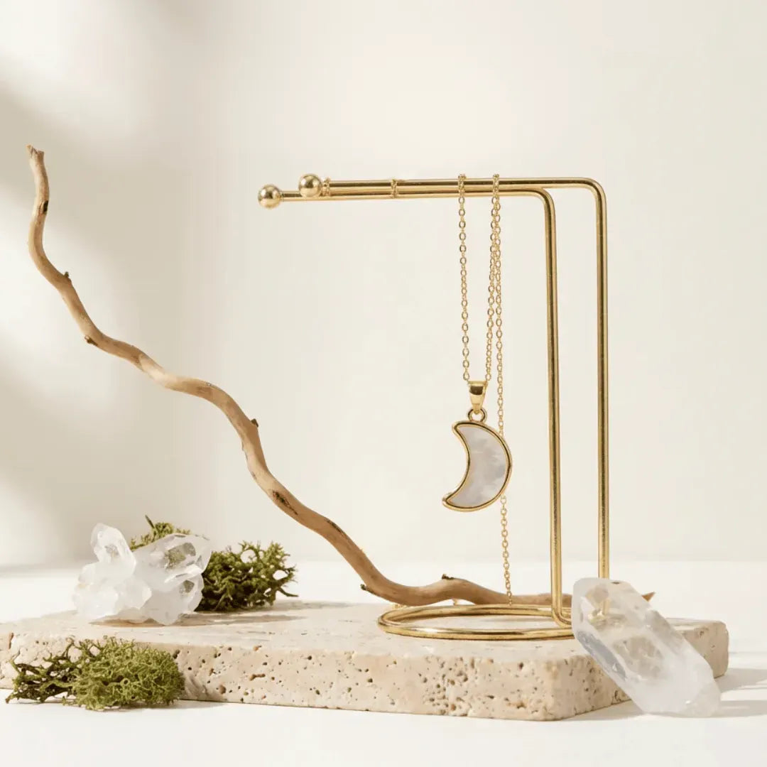 Gold necklace with a moon pendant on a decorative stand with natural elements.
