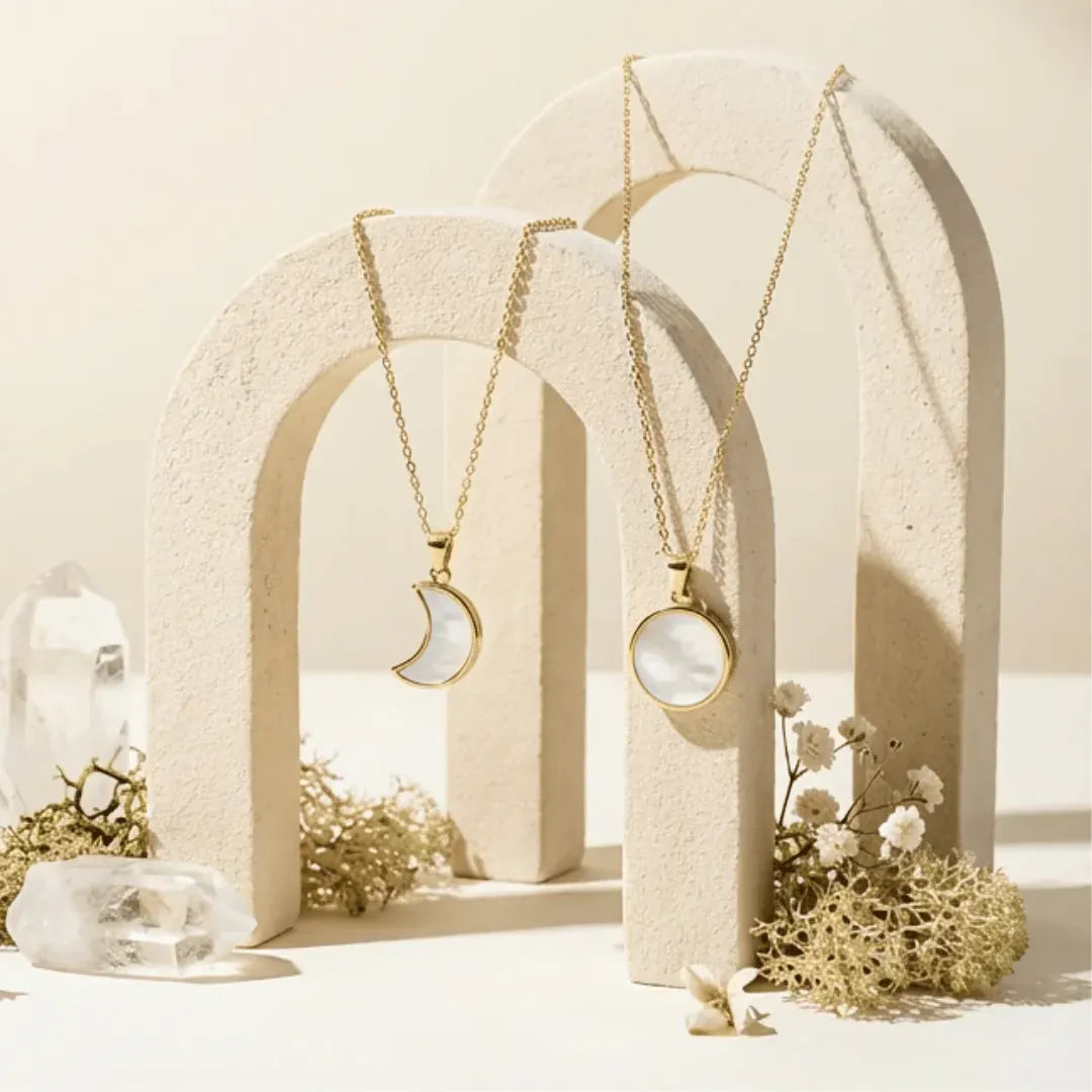 Two gold necklaces with moon and circle pendants on a neutral background