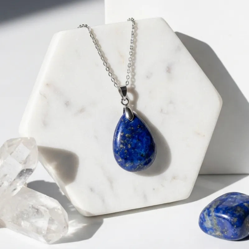 Necklace with a blue teardrop pendant on a marble stand with crystals around