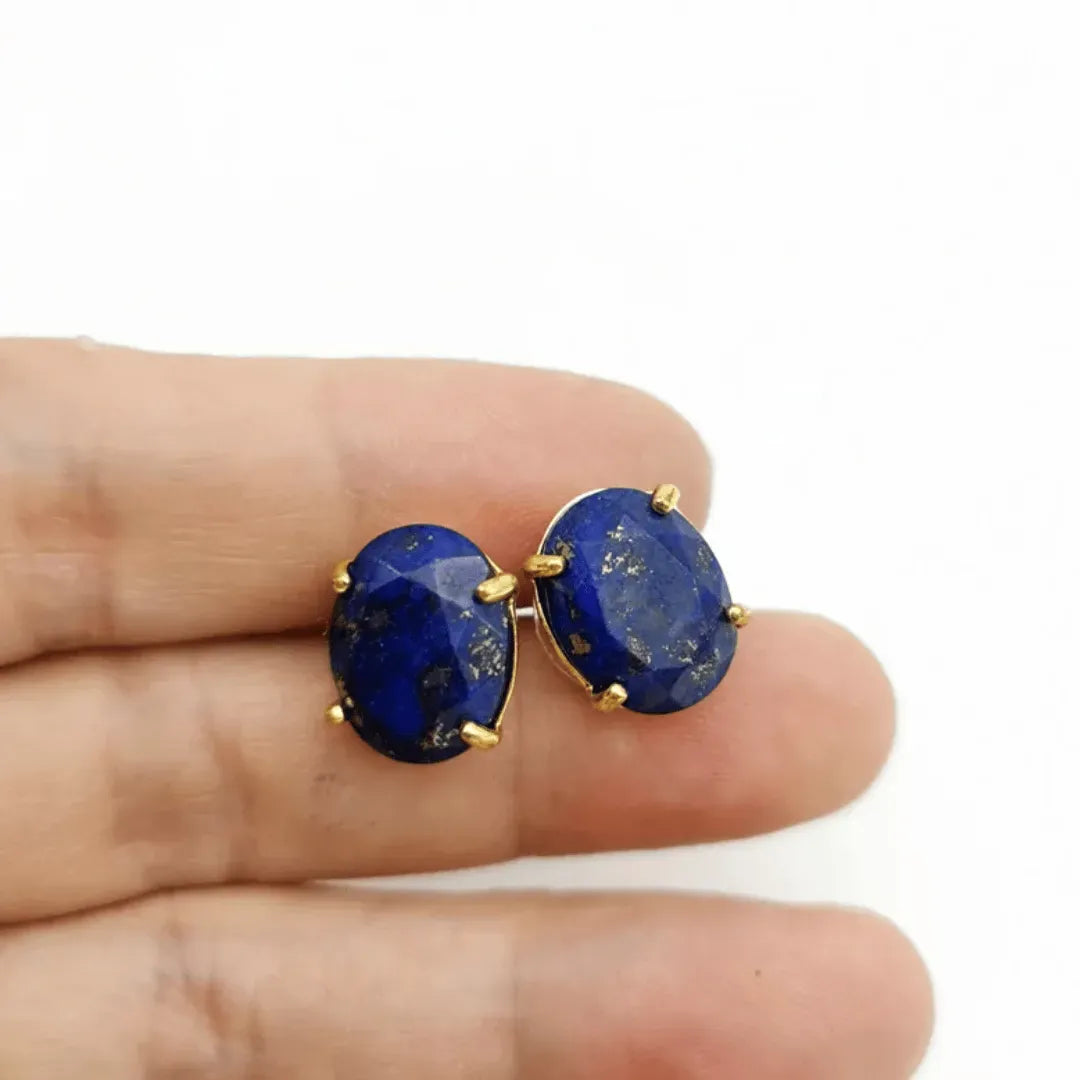 Lapis lazuli stud earrings with gold accents held between fingers on a white background