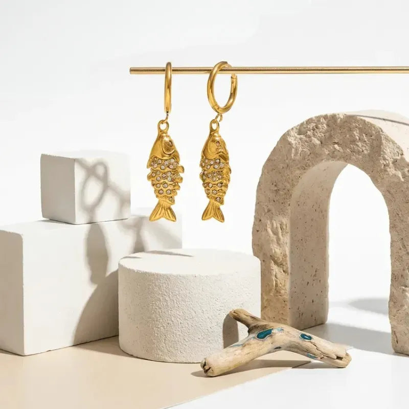 Gold fish-shaped earrings on a white background with architectural elements.