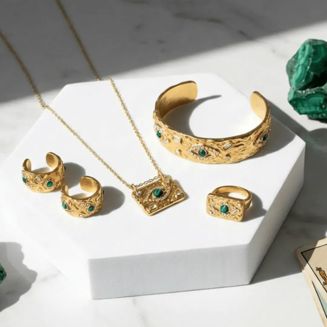 Gold jewelry set with emerald stones on a white surface