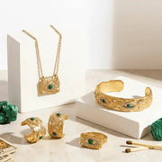 Gold jewelry set with green gemstones on a white surface