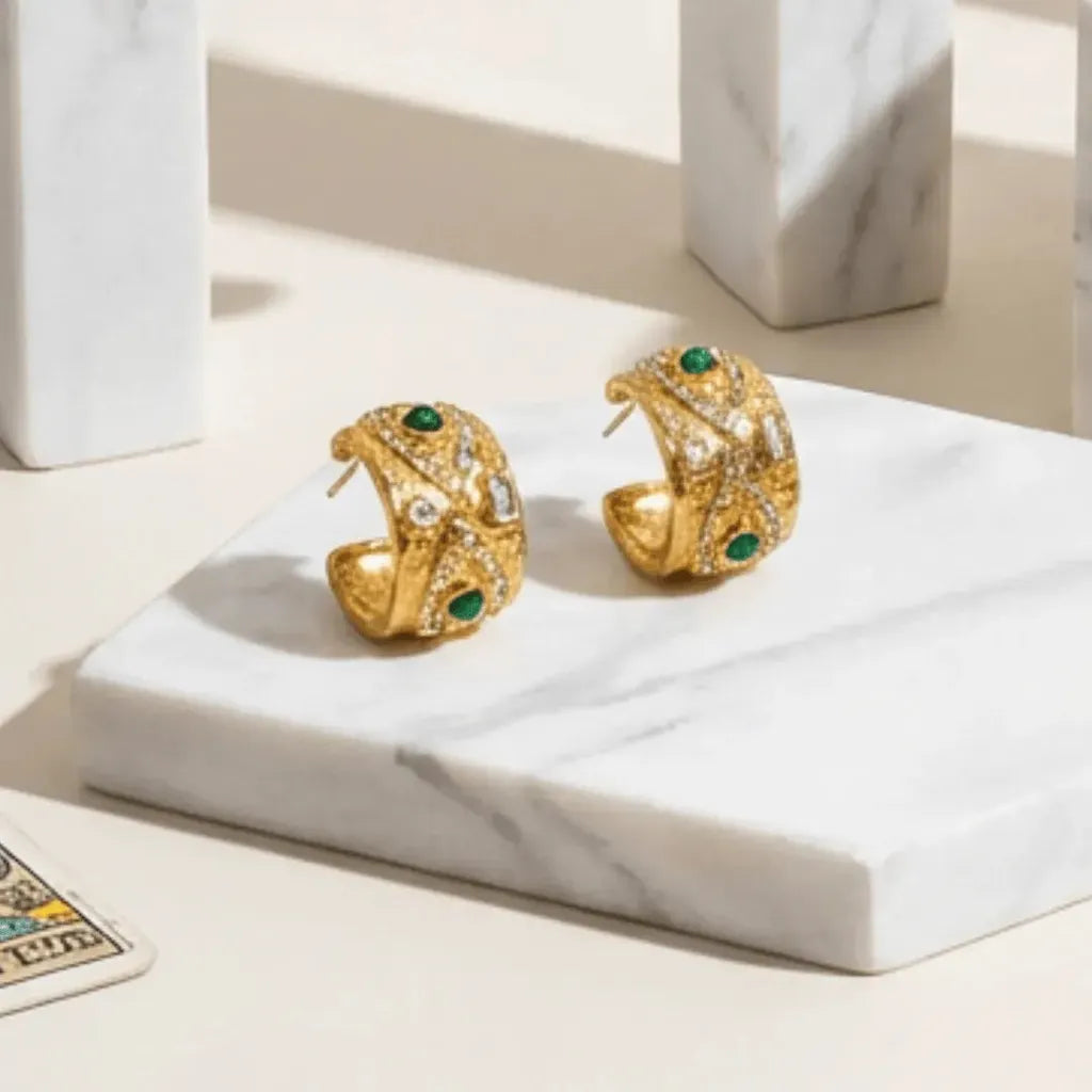 Gold earrings with green gemstones on a marble surface