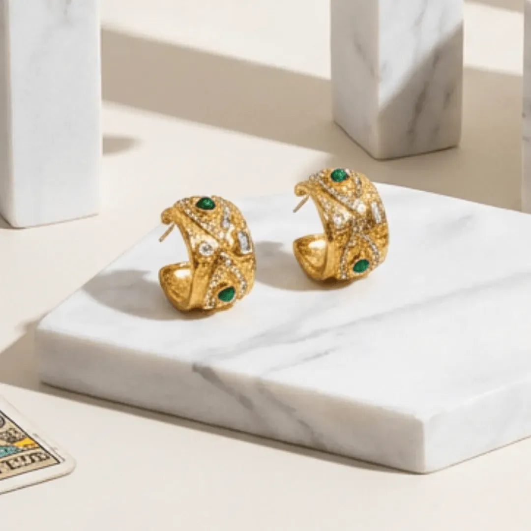 Gold earrings with green gemstones on a marble surface
