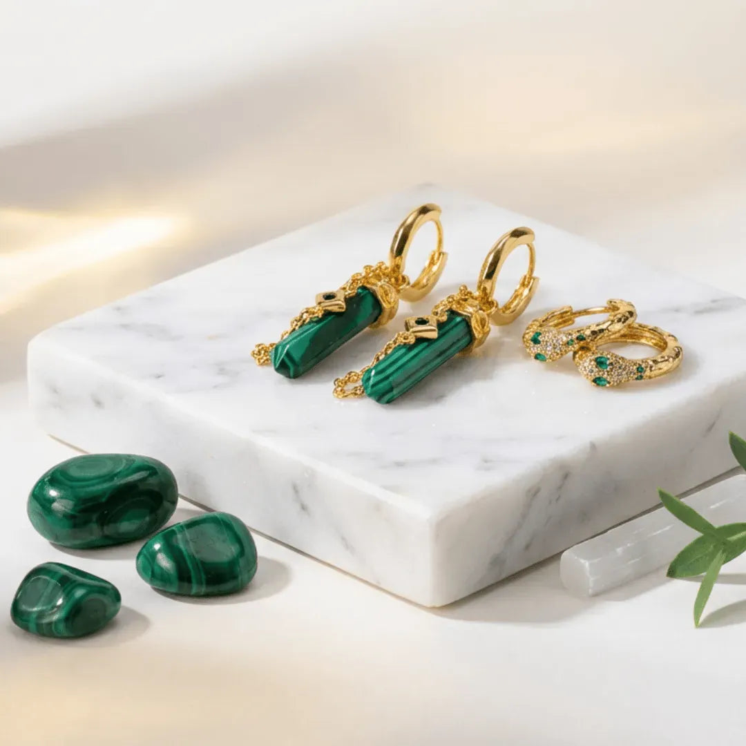 Gold earrings with green gemstones on a marble surface