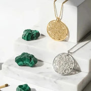 Gold and silver circular pendants with green stones on a white surface