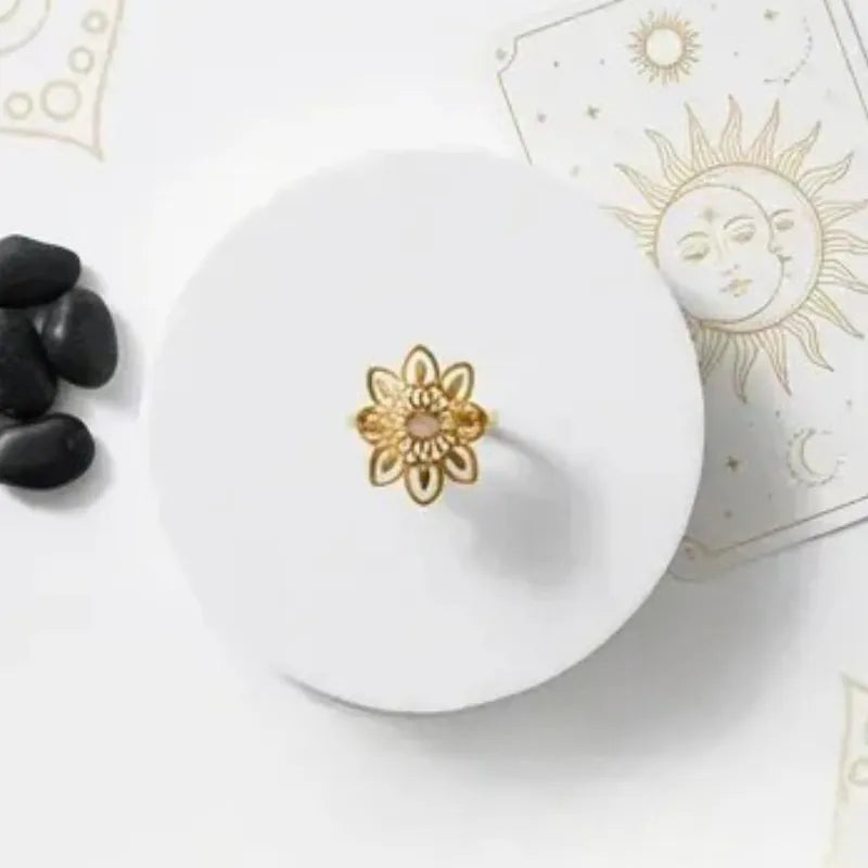 Gold ring on a white dish with black stones and a sun design in the background
