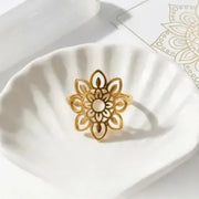 Gold floral ring on a white surface with a decorative background