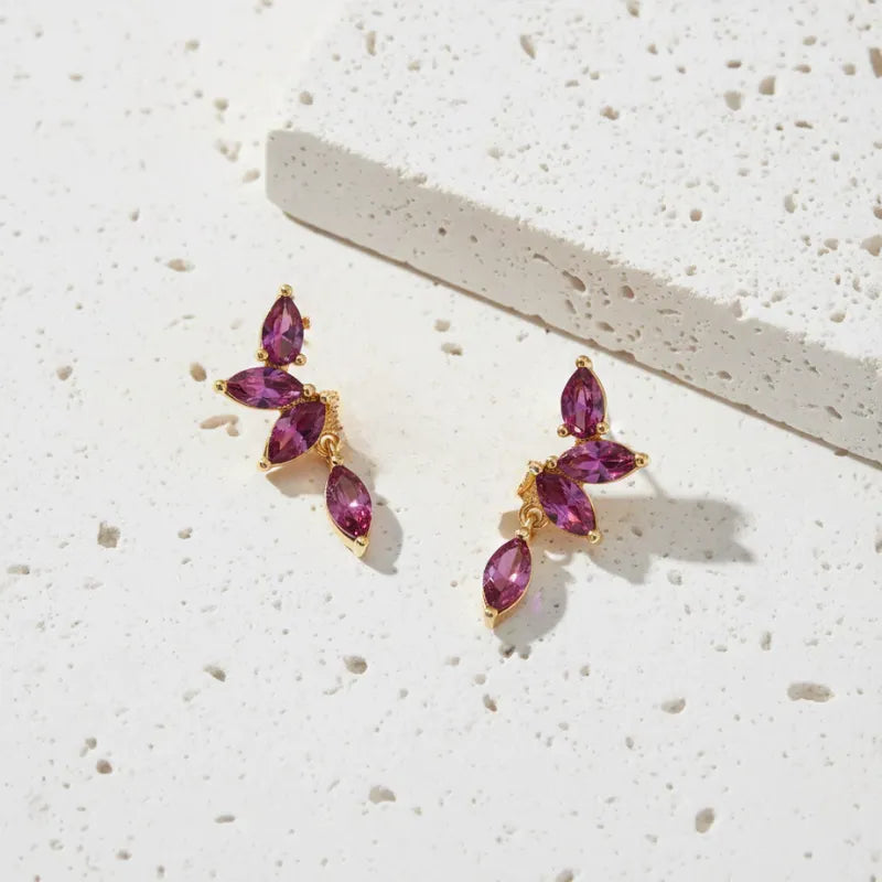 Gold earrings with purple gemstones on a light surface