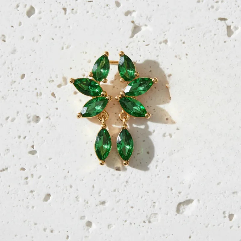 Gold earrings with green gemstones on a textured white background
