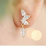 Gold and crystal earring worn on an ear with a blurred background